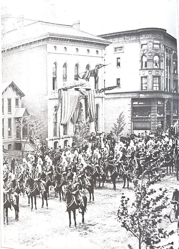 The Standard Club’s first clubhouse, draped with flags and bunting, as mounted riders in plumed helmets gather in the street in front of it.